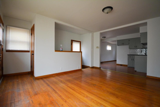 unfurnished living room featuring baseboards, a sink, and light wood finished floors