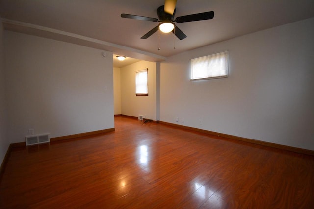 spare room with a ceiling fan, visible vents, baseboards, and wood finished floors