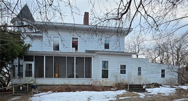 snow covered house with a sunroom and a chimney