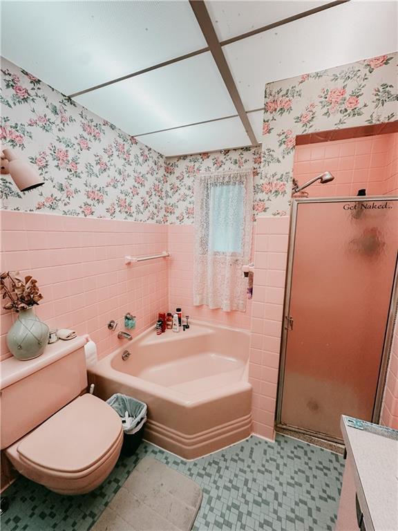 bathroom with a bath, wallpapered walls, a wainscoted wall, and a stall shower