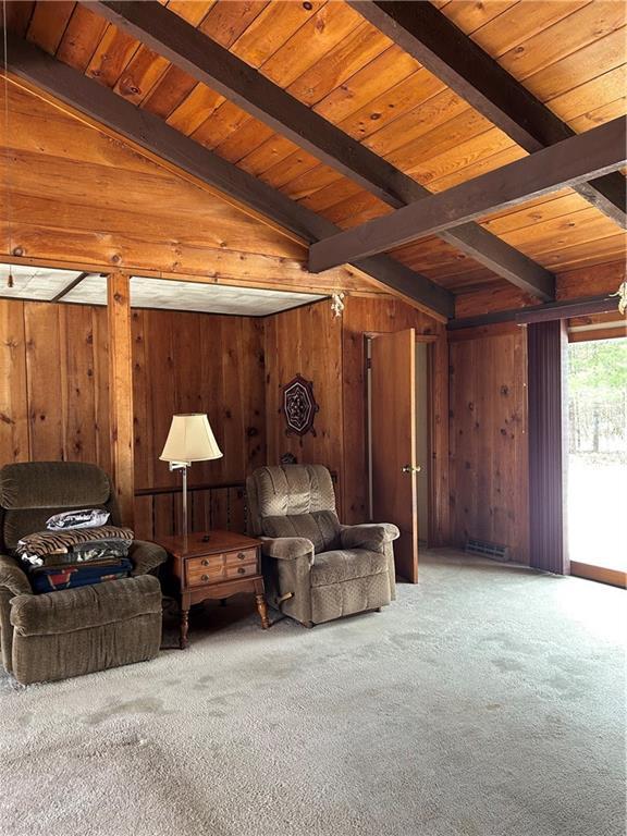 sitting room with beamed ceiling, carpet flooring, and wooden walls