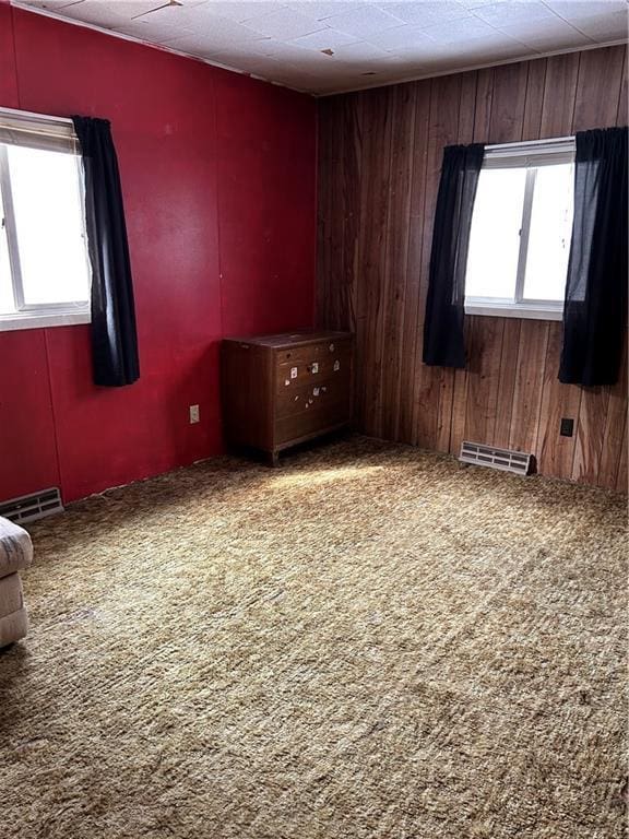 carpeted spare room featuring visible vents and wooden walls