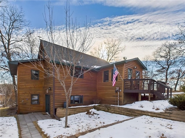 snow covered rear of property featuring log veneer siding and a wooden deck