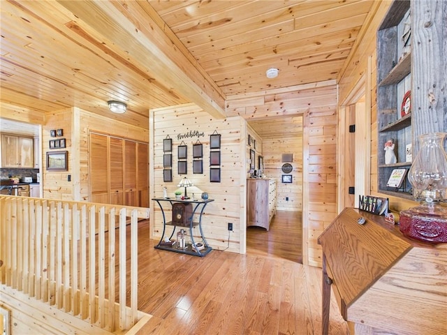 hall with light wood-style floors, wooden ceiling, wood walls, and an upstairs landing