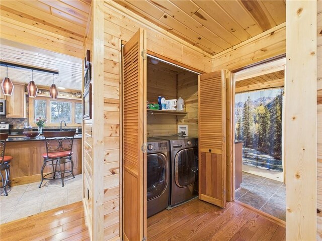 clothes washing area featuring laundry area, wooden walls, wooden ceiling, light wood-style flooring, and washer and dryer