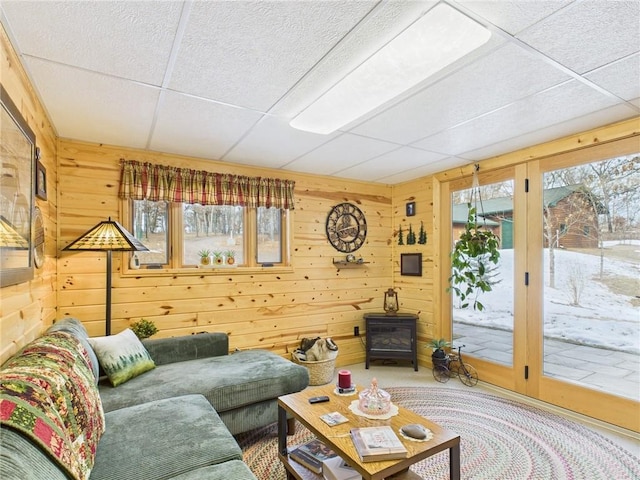 living area with a paneled ceiling, carpet, a wood stove, and wooden walls