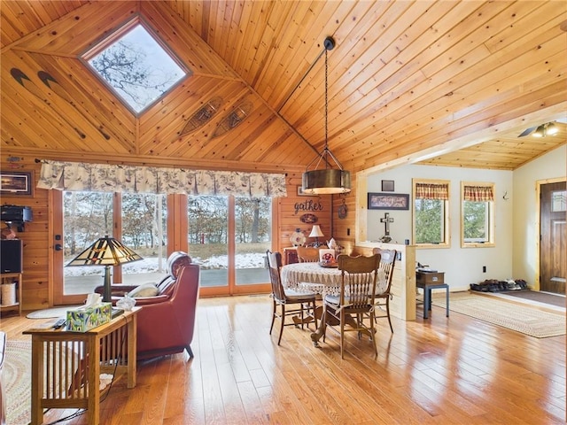 dining area with a skylight, wood-type flooring, wood ceiling, wooden walls, and high vaulted ceiling