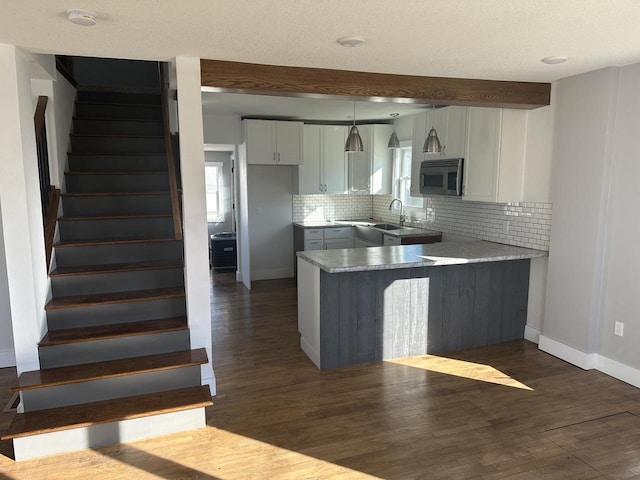 kitchen with a peninsula, dark wood-style floors, tasteful backsplash, and stainless steel microwave