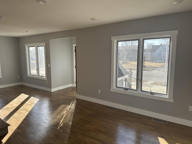 empty room featuring visible vents, dark wood finished floors, a textured ceiling, and baseboards