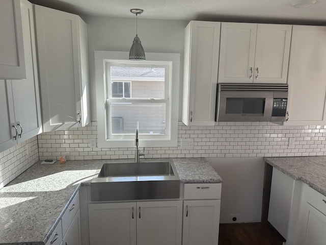 kitchen with decorative light fixtures, tasteful backsplash, stainless steel microwave, white cabinets, and a sink