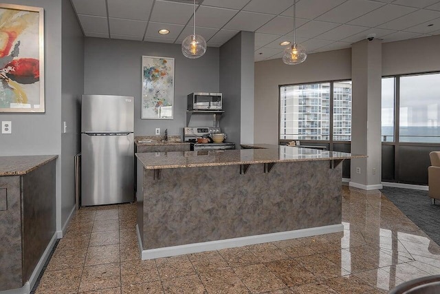 kitchen with a drop ceiling, granite finish floor, baseboards, appliances with stainless steel finishes, and pendant lighting