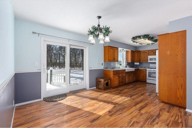 kitchen with brown cabinets, dark wood finished floors, light countertops, an inviting chandelier, and white appliances