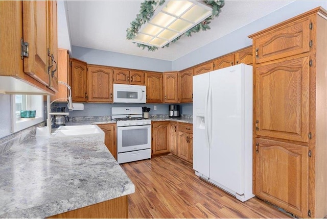 kitchen with white appliances, brown cabinets, a sink, and light countertops