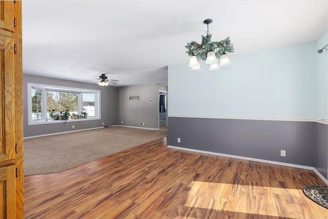 empty room with a textured ceiling, baseboards, wood finished floors, and ceiling fan with notable chandelier