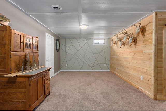 basement featuring wooden walls, light colored carpet, visible vents, and baseboards