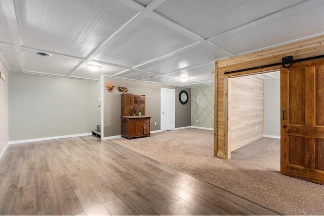 finished basement with a barn door, wooden walls, visible vents, baseboards, and light wood-style floors