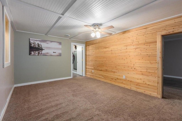 carpeted empty room featuring wood walls, a ceiling fan, and baseboards