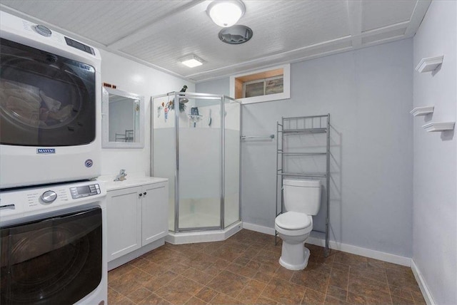 full bathroom with toilet, stacked washer and dryer, vanity, baseboards, and a shower stall