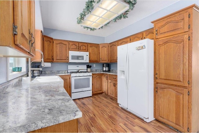 kitchen featuring white appliances, light wood-style flooring, brown cabinets, light countertops, and a sink