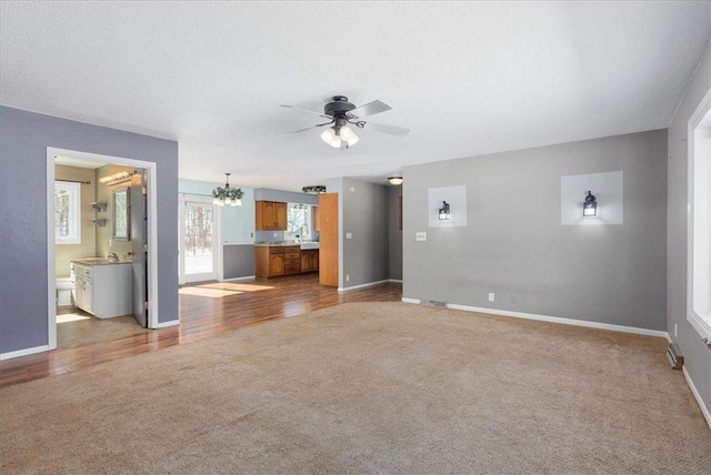 unfurnished living room featuring light carpet, baseboards, a textured ceiling, and ceiling fan with notable chandelier