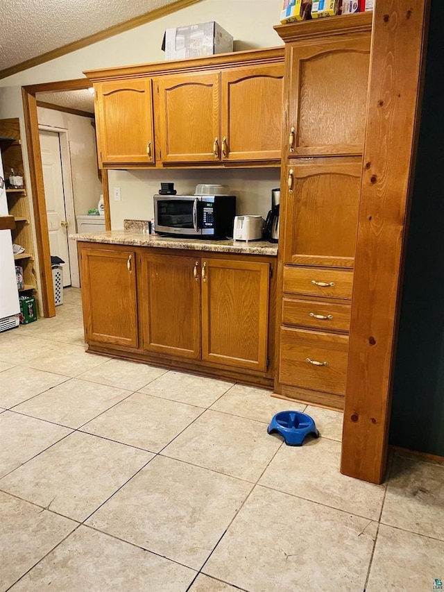 kitchen with vaulted ceiling, light tile patterned floors, stainless steel microwave, and brown cabinetry