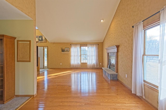 unfurnished living room featuring a wealth of natural light, light wood finished floors, a high end fireplace, and baseboards