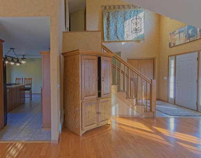 entryway with stairs, light wood-type flooring, a towering ceiling, and baseboards