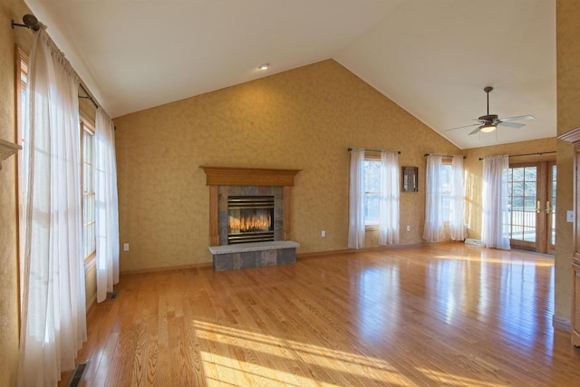 unfurnished living room with a tiled fireplace, ceiling fan, wood finished floors, high vaulted ceiling, and baseboards