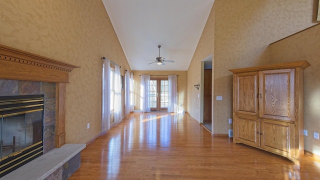 entryway featuring a ceiling fan, a tiled fireplace, french doors, light wood-type flooring, and high vaulted ceiling