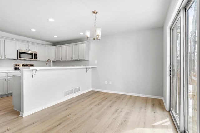 kitchen with a breakfast bar area, stainless steel appliances, light countertops, visible vents, and light wood-style flooring