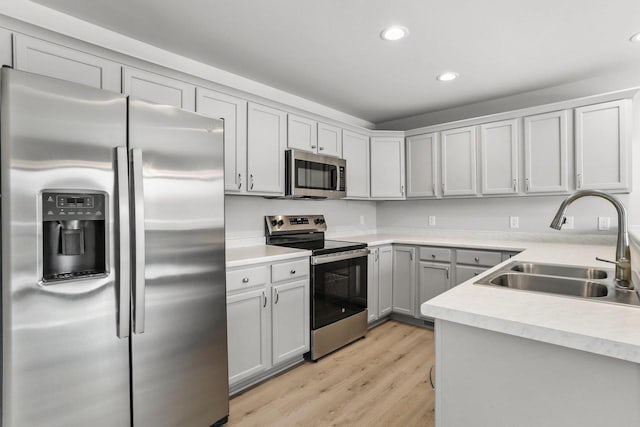 kitchen with recessed lighting, a sink, light countertops, appliances with stainless steel finishes, and light wood finished floors