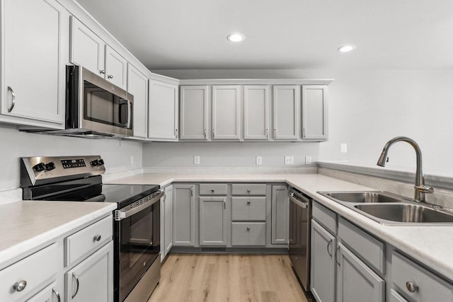 kitchen with stainless steel appliances, a sink, light countertops, gray cabinets, and light wood finished floors