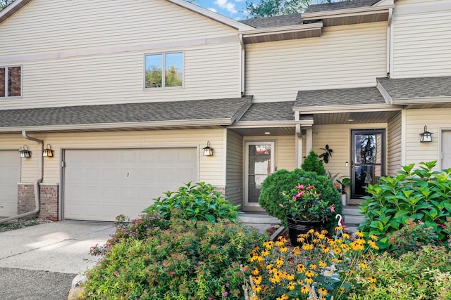 multi unit property featuring a garage, concrete driveway, brick siding, and roof with shingles