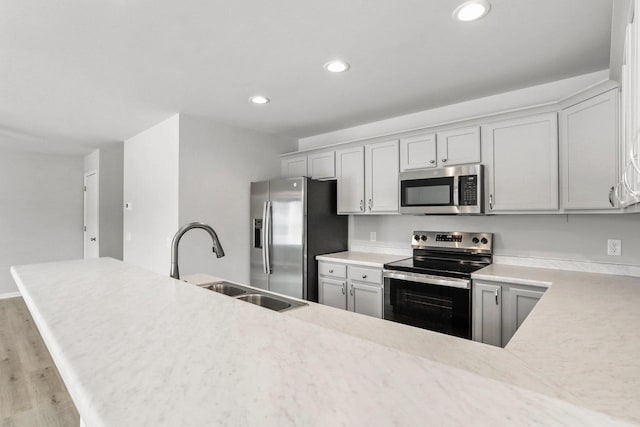 kitchen featuring stainless steel appliances, recessed lighting, light countertops, a sink, and wood finished floors