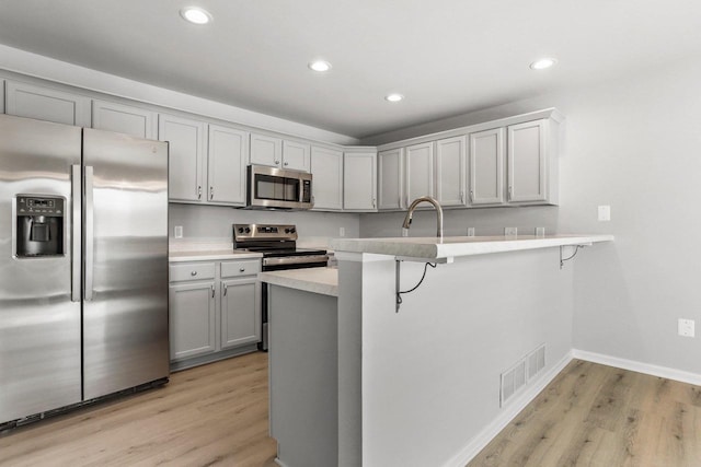 kitchen with a breakfast bar area, gray cabinetry, stainless steel appliances, visible vents, and light countertops