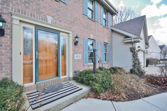 entrance to property featuring brick siding, a shingled roof, and a garage