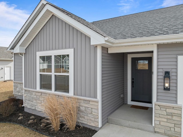 entrance to property featuring board and batten siding, stone siding, and roof with shingles