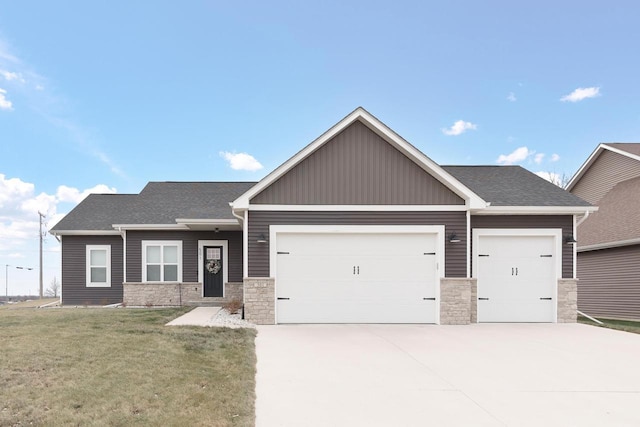 view of front of home featuring a garage, a shingled roof, concrete driveway, stone siding, and a front yard