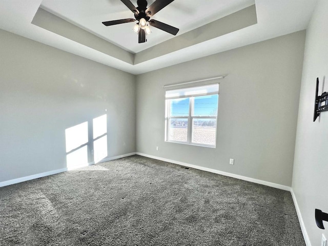 unfurnished room featuring ceiling fan, carpet flooring, a raised ceiling, and baseboards