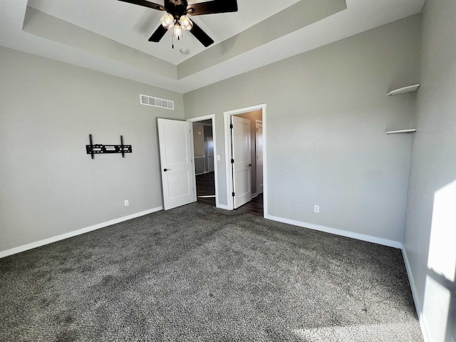 unfurnished bedroom featuring dark colored carpet, a tray ceiling, visible vents, and baseboards