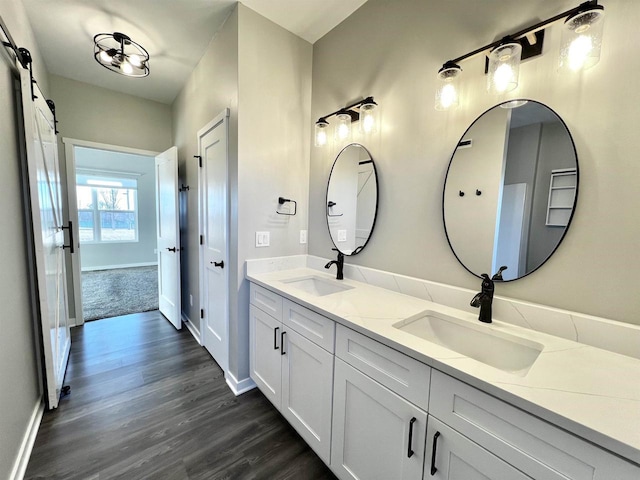 full bath featuring double vanity, a sink, baseboards, and wood finished floors