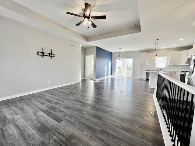 unfurnished living room featuring baseboards, visible vents, a raised ceiling, dark wood-type flooring, and ceiling fan with notable chandelier