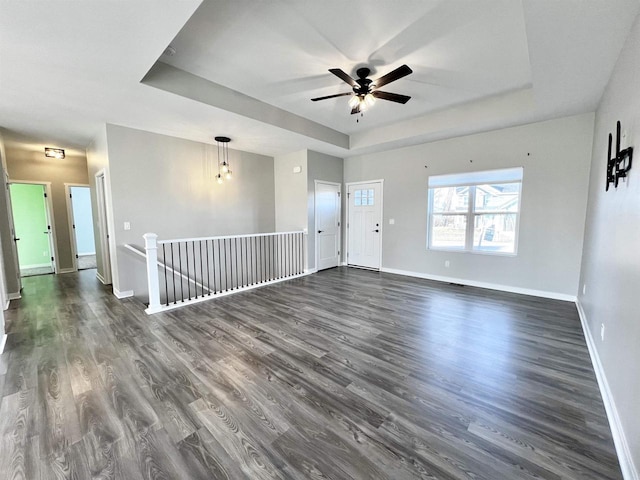 spare room featuring dark wood-style floors, baseboards, a tray ceiling, and a ceiling fan