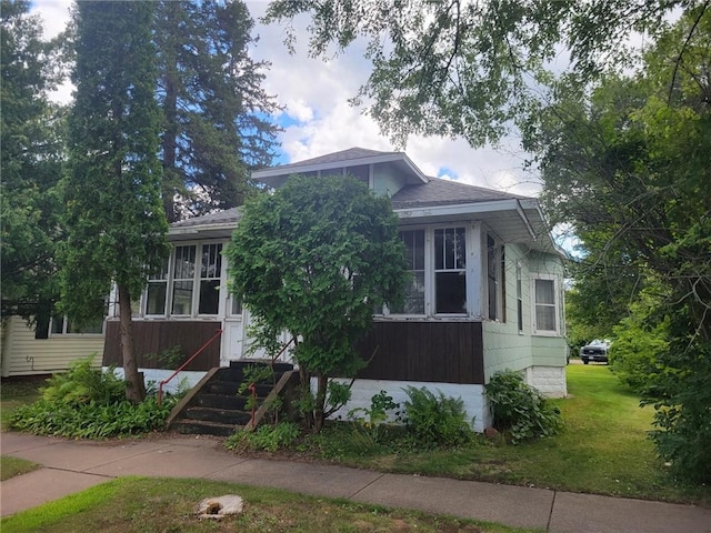 view of front of property featuring a shingled roof, a front yard, a sunroom, and entry steps