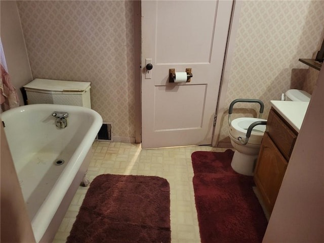 bathroom featuring wallpapered walls, toilet, tile patterned floors, vanity, and a freestanding tub