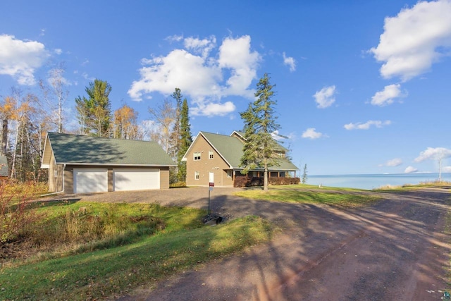 view of front of property with dirt driveway, a water view, and a detached garage