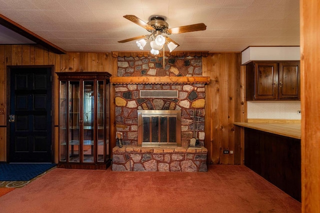 unfurnished living room with carpet, a stone fireplace, and wooden walls