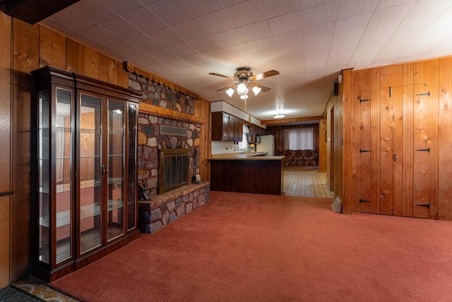 unfurnished living room featuring wood walls, a fireplace, a ceiling fan, and carpet flooring