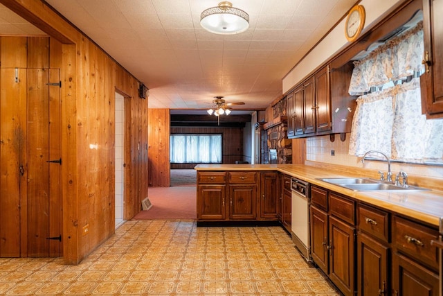 kitchen with white dishwasher, wood walls, a sink, a ceiling fan, and light countertops