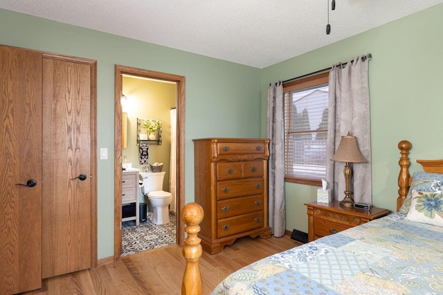 bedroom with a textured ceiling, light wood finished floors, and ensuite bathroom